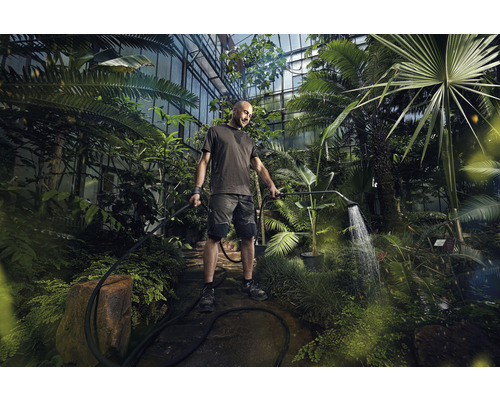 Un homme arrose des plantes dans une serre avec une douche de jardin.