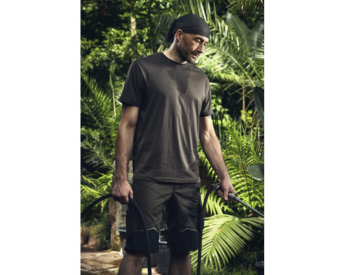 Un homme en vêtements de travail tient un tuyau d''arrosage dans un jardin.