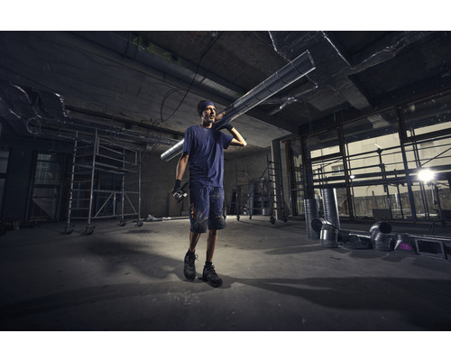 Un homme porte un conduit de ventilation sur un chantier.