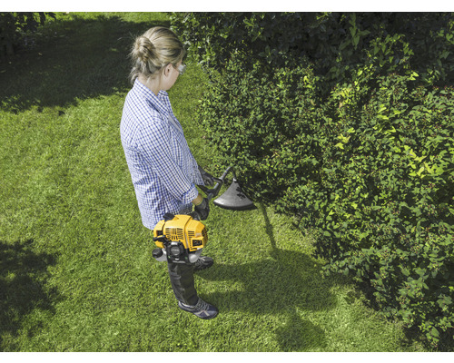 Une femme travaille avec un coupe-bordure jaune dans le jardin.