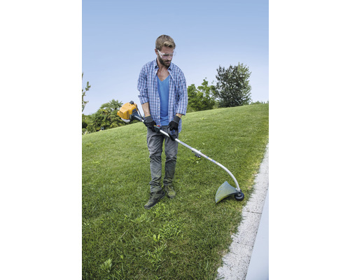 Un homme coupe du gazon avec un coupe-bordures dans un jardin.