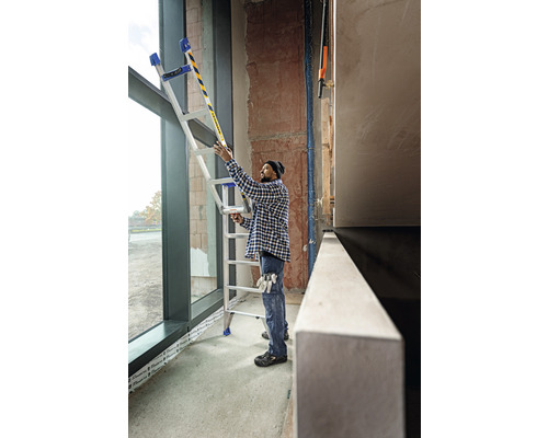 Une personne utilise une échelle multifonctionnelle près d''une fenêtre sur un chantier.