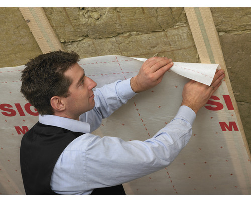 Un homme fixe un écran pare-vapeur sur une structure de toit.