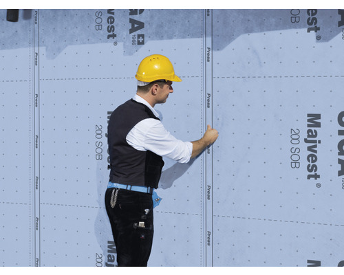 Un ouvrier du bâtiment fixe un écran de façade Majvest 200 SOB sur un mur.