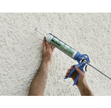 Photo extérieure d''une personne appliquant du mastic sur un mur avec un pistolet à cartouche