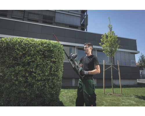 Un homme taille une haie avec un taille-haie dans le jardin.
