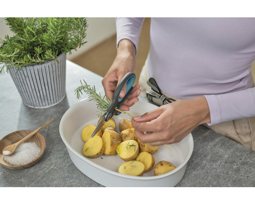 Person schneidet Rosmarin mit einer Schere über einer Schüssel mit Kartoffeln.