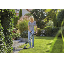 Frau benutzt Rasentrimmer im Garten zur Rasenpflege.