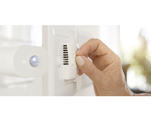 Une main actionne un thermostat pour régler la température.