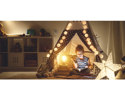 Fille lisant dans une tente étoilée avec guirlande lumineuse et lampe, peluche dans la pièce