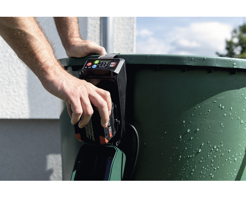 Un homme installe une batterie dans une pompe pour réservoir d''eau de pluie.