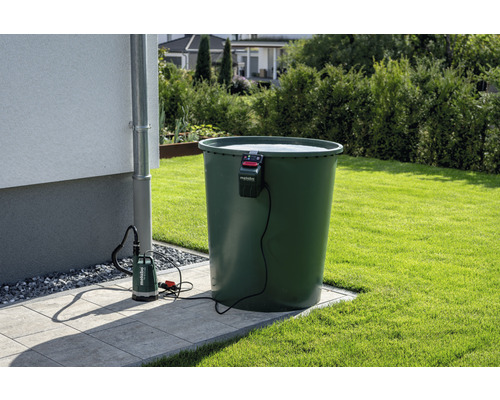 Scène de jardin avec récupérateur d''eau de pluie, mur de maison, tuyau de descente pluviale et pompe submersible avec logo Metabo