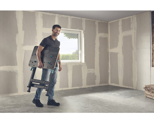 Mann trägt eine Wolfcraft Master 650 Werkbank in einem Raum mit Trockenbauwänden