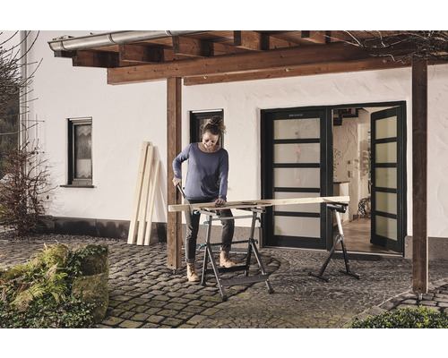 Frau sägt Holz auf einer klappbaren Werkbank im Freien.