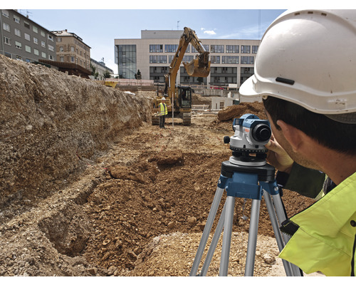 Un ouvrier du bâtiment portant un casque utilise un niveau optique sur un chantier.