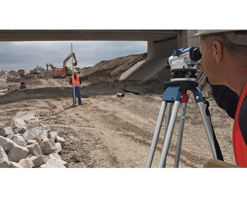 Ouvriers du bâtiment effectuant des travaux de topographie avec un niveau optique sur un chantier.