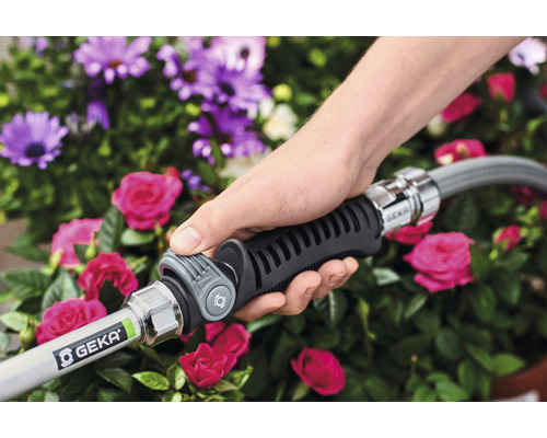 Eine Hand hält einen Gartenschlauch mit GEKA-Kupplung vor Blumen