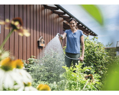 Frau bewässert Garten mit Gartenschlauch und Sprühkopf.