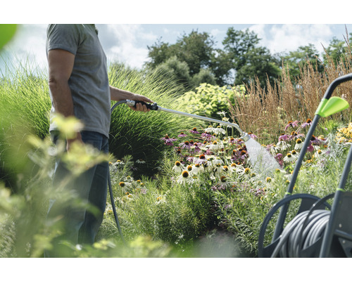 Eine Person bewässert Blumen im Garten mit einer Gartenspritze.