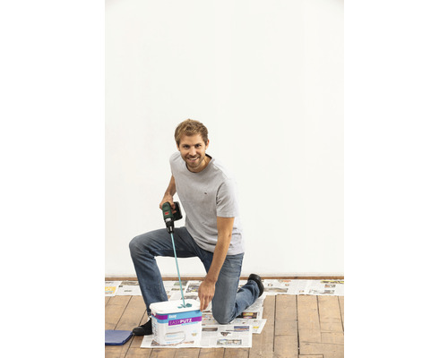 Un homme agenouillé devant un seau d''enduit prêt à l''emploi utilise un outil de mélange pour mélanger.