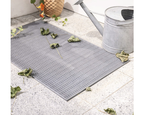 Paillasson gris avec motif quadrillé à côté d''un arrosoir et de plantes