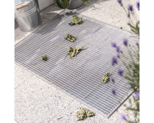 Caillebotis gris avec feuilles sur pavés