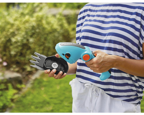 Une personne tient une cisaille à gazon sans fil Gardena avec une tête de lame interchangeable.