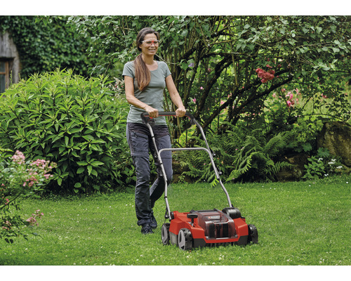 Une femme utilise un scarificateur dans le jardin.