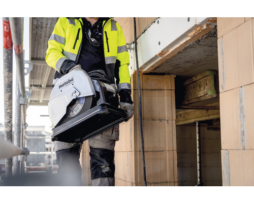 Un ouvrier du bâtiment porte une scie à matériaux Metabo sur un chantier.