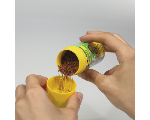 Des mains versent de la nourriture pour insectes JBL dans un couvercle jaune