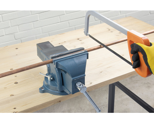 Eine Rohrzange hält ein Kupferrohr, das mit einer Metallsäge geschnitten wird.