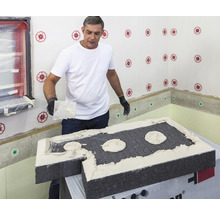 Mann trägt Dämmstoffkleber auf eine Dämmplatte auf. Dämmstoffplatten werden an einer Wand mit Dämmstoffdübel befestigt.