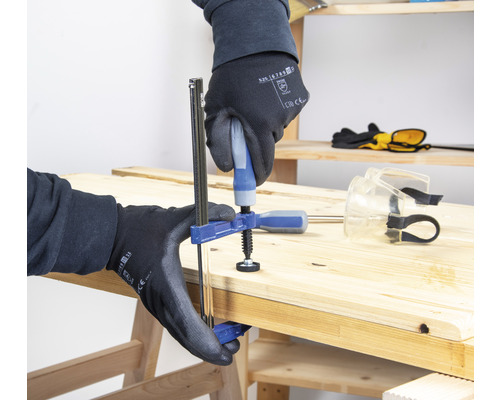Une personne fixe une pièce de bois avec un serre-joint à une main.