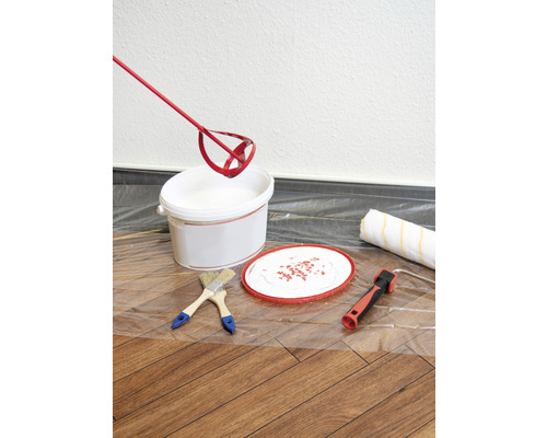 Seau de peinture, mélangeur de peinture, pinceaux et rouleau à peinture sur un film de protection pour travaux de peinture