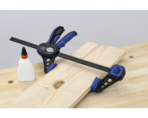 Serre-joint serre une planche de bois sur un établi à côté d''un flacon de colle à bois