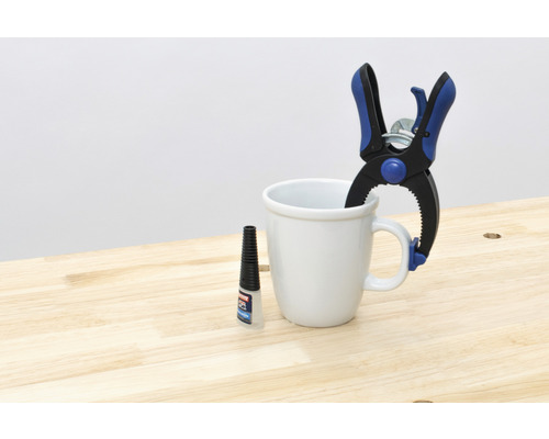 Federzwinge, Klebstoff und Tasse auf Holztisch