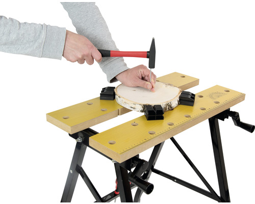 Person nagelt mit einem Hammer einen Nagel in ein Holzstück, das mit einer Werkbank befestigt ist.