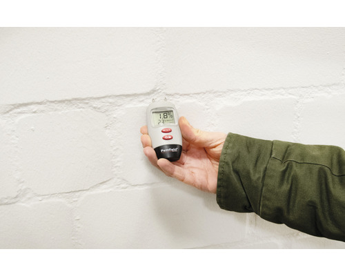 Feuchtigkeitsmesser in Hand vor einer Wand