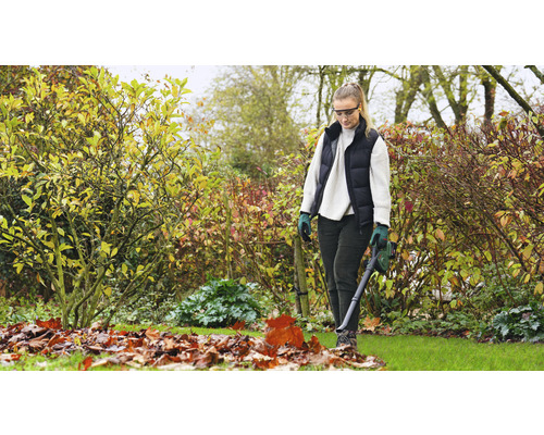 Une femme utilise un aspirateur de feuilles dans le jardin pour enlever les feuilles mortes.