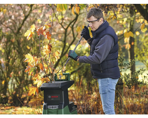 Un homme utilise un broyeur de végétaux pour déchiqueter des branches.