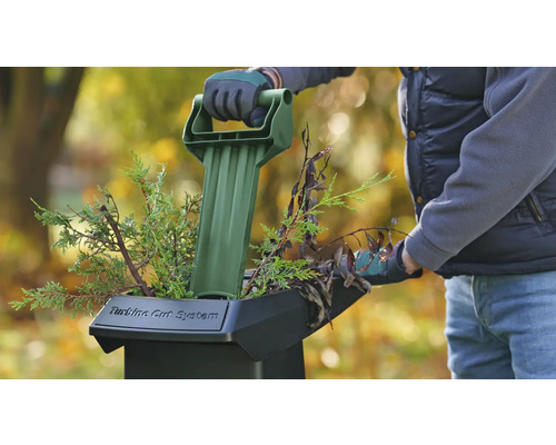 Une personne utilise un broyeur de jardin pour broyer des branches et des brindilles.