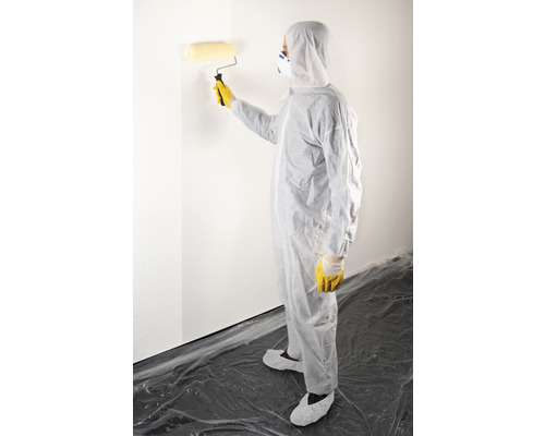 Personne en tenue de protection peignant un mur avec un rouleau.