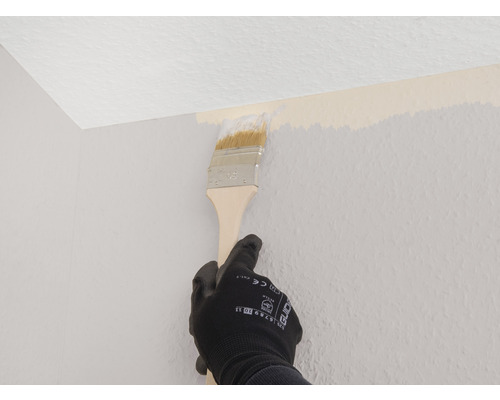 Une personne peint un mur dans une pièce avec un pinceau.