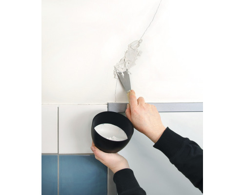 Eine Person verschliesst mit einem Spachtel einen Riss in der Wand. Eine Schale mit Füllmaterial wird gehalten.
