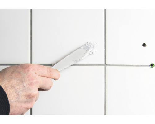 Auftragen von Fugenmasse mit einem Spachtel auf Fliesen
