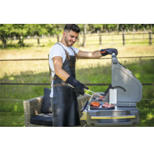 Mann grilliert im Garten mit Grill, Grillzange, Grillschürze und Grillhandschuhen