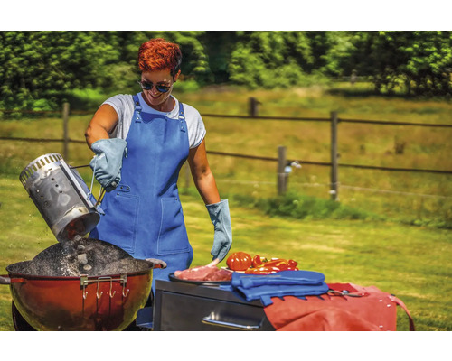 Une femme vide du charbon de bois d''une cheminée d''allumage dans un barbecue tout en portant un tablier et des gants de barbecue
