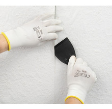 Personne lisse le papier peint avec une spatule et des gants de protection