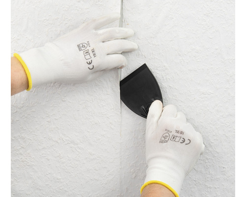 Personne lisse le papier peint avec une spatule et des gants de protection