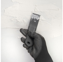 Main gantée avec spatule enduisant un mur